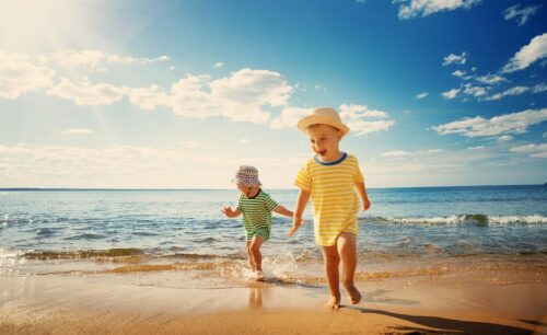 Ägypten Urlaub 2024 buchen in Erfurt bei REISEBÜRO Wache; im Bild: zwei kleine Kinder mit Sonnenhüten und T-Shirts am Strand, dahinter das Meer, über ihnen blauer Himmel mit Wölkchen