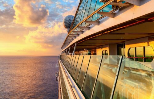 Kreuzfahrt Tipps für die Kabinen Kategorie vom REISEBÜRO Wache; im Bild: die spiegelnden Fenster an der Seite eines Kreuzfahrtschiffs, das auf dem Meer unterwegs ist, Sonnenuntergang am Bildrand