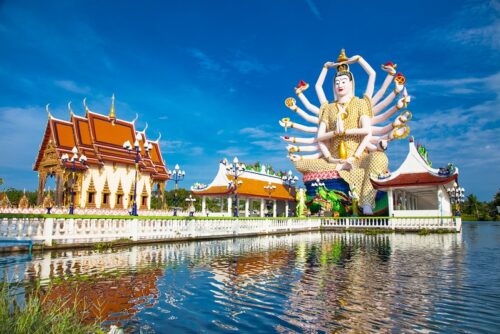 Thailand Urlaub buchen Erfurt; im Bild: der Tempel Wat Plai Laem auf Koh Samui, eine riesige 18-armige Buddha-Statue umgeben von Tempel-Häusern mit Dächern, die leicht nach oben gebogen auslaufen